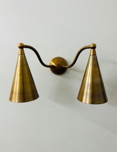 two brass wall lights with curved arms and one light on the opposite side, against a white background