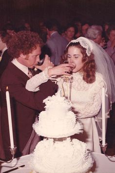 a bride and groom feeding each other cake at their wedding reception with candles in the background