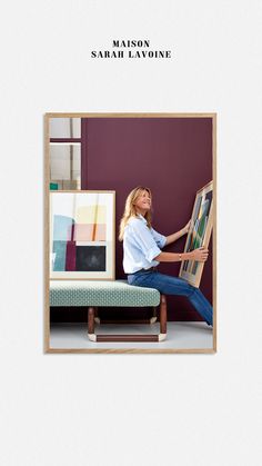 a woman sitting on top of a bench in front of a wall with pictures and furniture