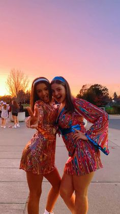 two young women posing for the camera with their arms around each other in front of a sunset