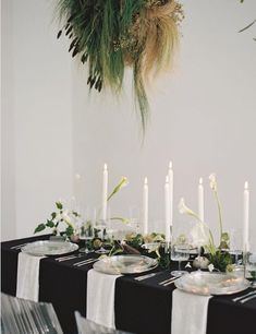 the table is set with black and white linens, greenery, candles, and plates