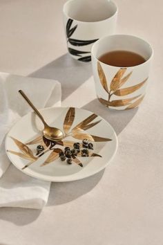 two coffee cups with spoons sitting next to each other on a white table cloth