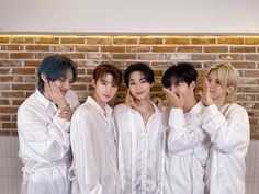 four young men in white robes posing for a photo with their hands on their faces