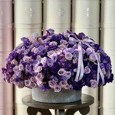 purple flowers are in a gray vase on a table next to stacks of white books