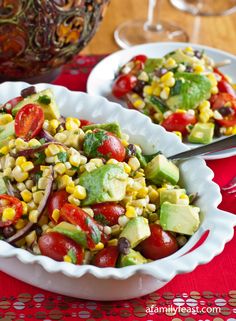 two white bowls filled with salad on top of a red table cloth next to silverware