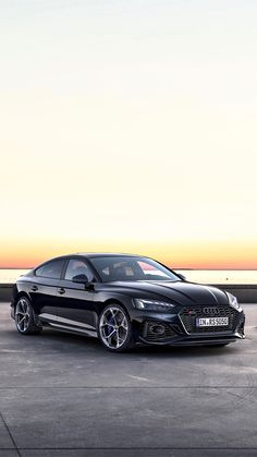 a black sports car parked in front of the ocean at sunset or dawn with its lights on