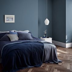 a bedroom with blue walls and wood flooring is pictured in this image, there are two lamps hanging above the bed