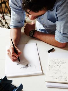 a man sitting at a table writing on a piece of paper with an ink pen