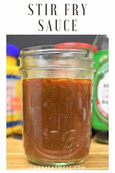 a mason jar filled with stir fry sauce on top of a wooden table next to other jars