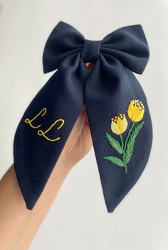 a hand holding up a blue bow with yellow flowers on it and the word love written in gold thread