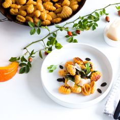 a white plate topped with pasta next to an orange and some other food on a table