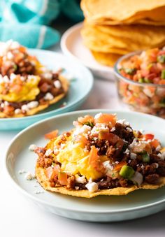 two plates with mexican food on them and some tortillas in the back ground