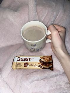 a person holding a cup of coffee next to a bar of chocolate on a pink blanket