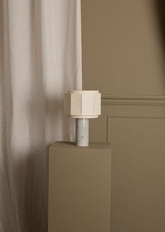 a white lamp sitting on top of a table next to a curtained window in a room