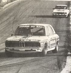 an old photo of two cars on a race track, one is white and the other is black