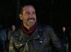 a man wearing a black leather jacket and red scarf smiles at the camera while standing in front of a crowd