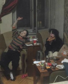 two people sitting on couches in a living room with one holding up his hand