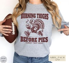 a woman holding a football and wearing a sweatshirt that says burning thighs before pies