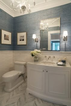 a bathroom with blue walls and white fixtures on the vanity, along with a chandelier