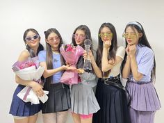 four girls are holding flowers and posing for the camera with glasses on their faces while one girl holds a bouquet in front of her face