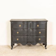 an antique black dresser with brass knobs on the top and bottom, against a white wall