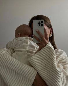 a woman taking a selfie with her cell phone while holding a baby in her arms