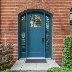 a blue front door on a brick building with green bushes and shrubbery around it