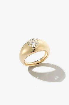 a gold ring with a diamond in the center and a shadow on the ground behind it