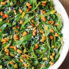 a white bowl filled with spinach and pine nuts on top of a wooden table