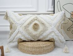 a white pillow with tassels on it sitting on top of a wicker basket