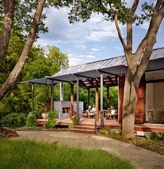 a small wooden cabin in the middle of some trees and grass with people sitting on it