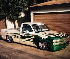 a green and white truck with flames painted on it's hood parked in front of a garage