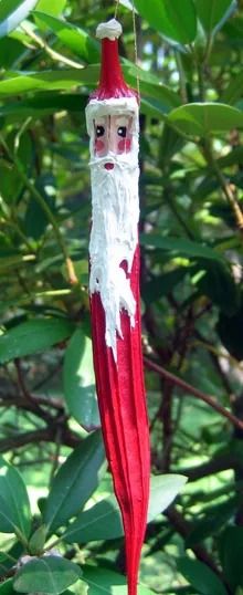 a red and white santa clause ornament hanging from a tree with green leaves