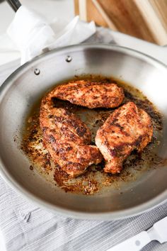 two pieces of meat in a frying pan on top of a white table cloth