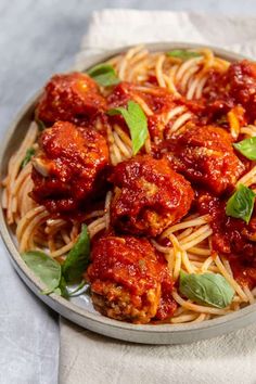 a plate full of spaghetti and meatballs with basil leaves on the side, ready to be eaten