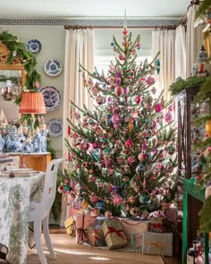 a decorated christmas tree in the corner of a dining room with plates on the table