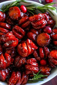 a bowl filled with cranberries and rosemary sprigs on top of a wooden table