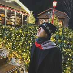 a woman wearing a hat and scarf standing in front of a christmas tree at night