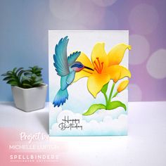 a birthday card with a hummingbird and yellow flower in the middle, on a table next to a potted plant