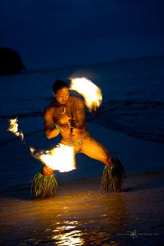 a woman is dancing on the beach with fire in her hands and holding two torches