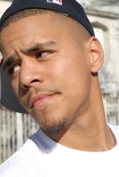 a close up of a person wearing a hat and looking off to the side with a building in the background