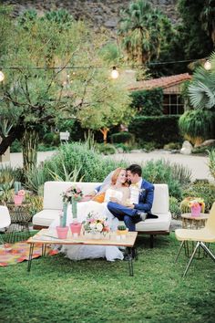 a bride and groom sitting on a couch in the middle of an outdoor garden area