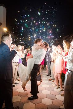 a bride and groom are kissing in front of their guests as fireworks go off behind them