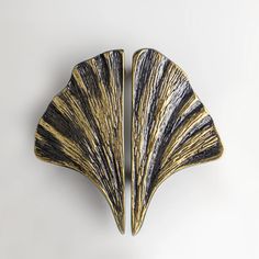 two gold and black fan shaped brooches on a white background