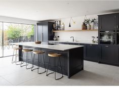 a kitchen with black cabinets and stools next to a sliding glass door that leads outside