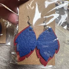 a pair of blue and red leaf shaped earrings on a piece of cardboard next to a plastic package