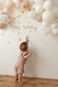 a baby standing in front of a wall with balloons