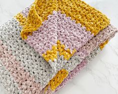 three crocheted blankets are stacked on top of each other, one is yellow and the other is pink