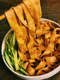 a bowl filled with noodles and vegetables on top of a wooden table next to chopsticks