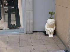 a stuffed animal sitting on the ground next to a door with a plant growing out of it